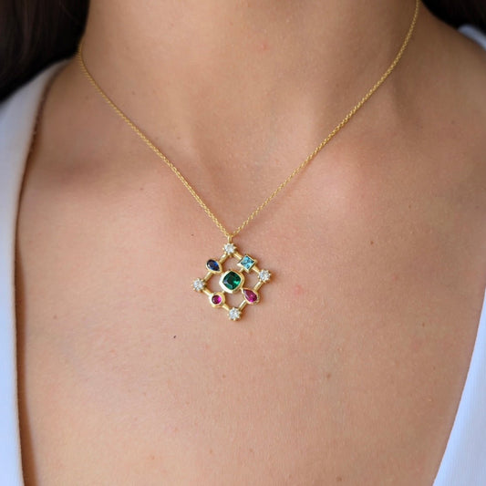 A gold-colored pendant necklace with a geometric croissant-shaped design featuring multiple colored gemstones, displayed on a person.