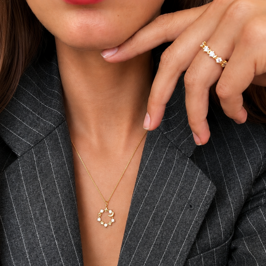 Close-up of a person wearing a gold necklace and ring, with a gray pinstripe blazer.