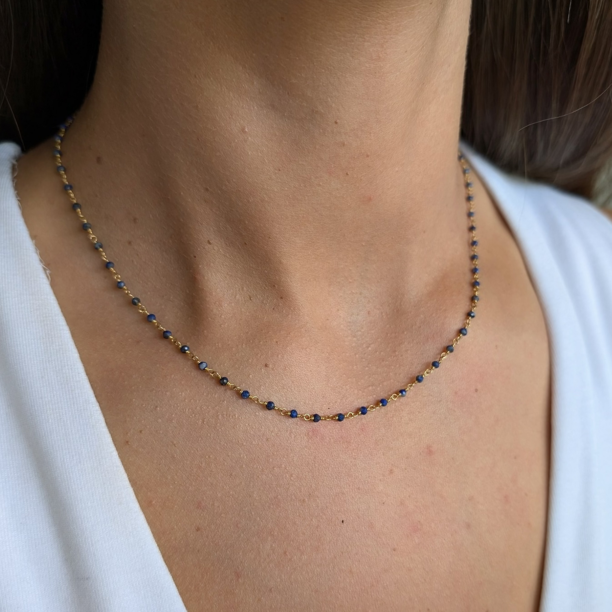 A person wearing a gold-colored necklace with round lapis lazuli gemstones.