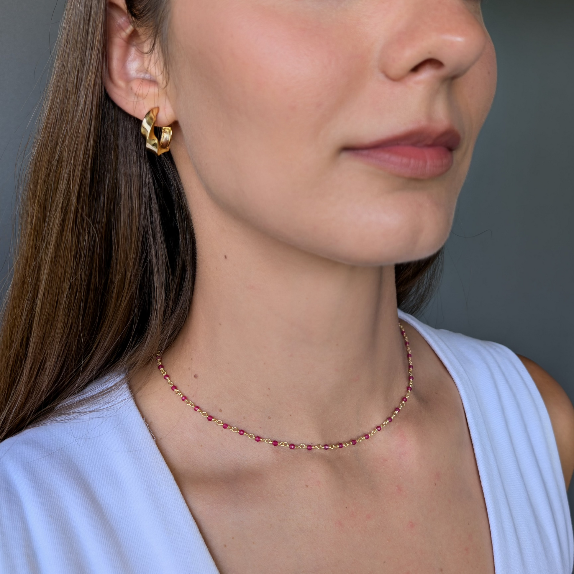 A person wearing a gold-plated brass necklace with pink calcite gemstones.